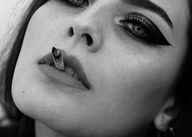 Retrato monocromático dramático de uma mulher com maquiagem ousada e cigarro, capturando intensidade.